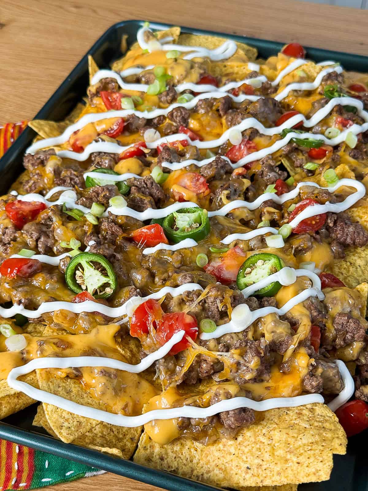 Tray of freshly baked sheet pan nachos with sliding cheese and toppings