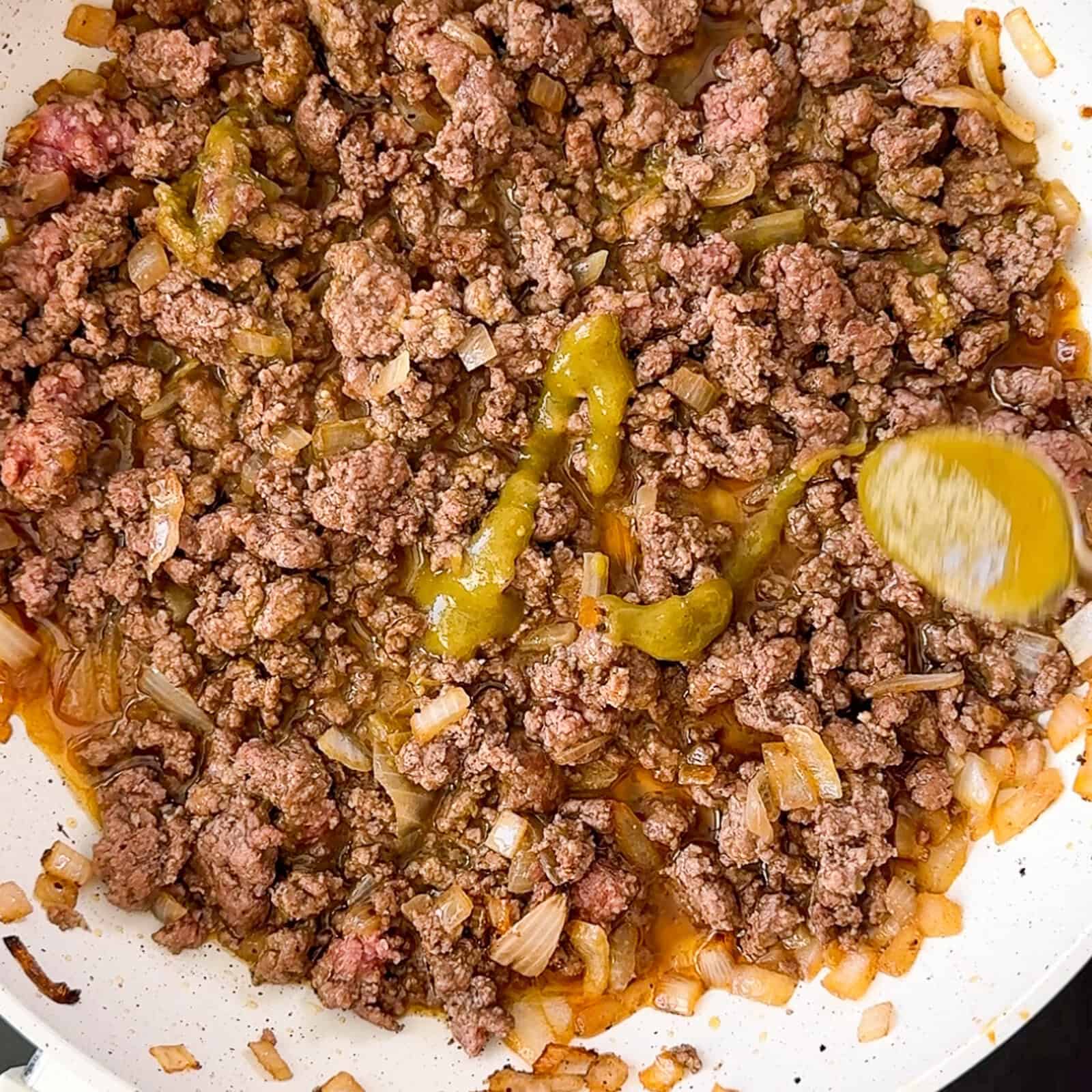 Adding salsa verde to ground beef cooking in a skillet for taco meat