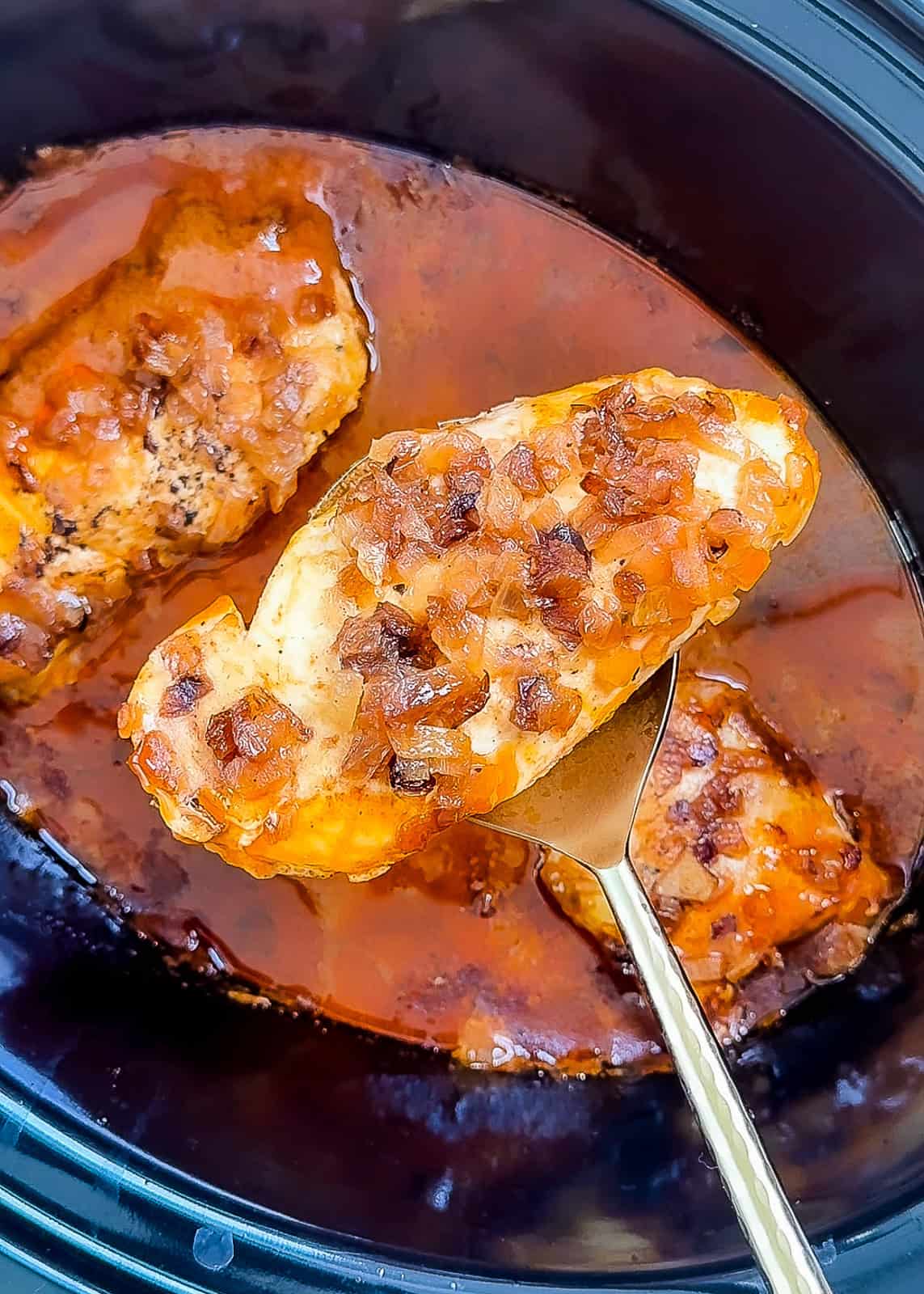Chicken breast with butter masala sauce and onions cooking in crockpot