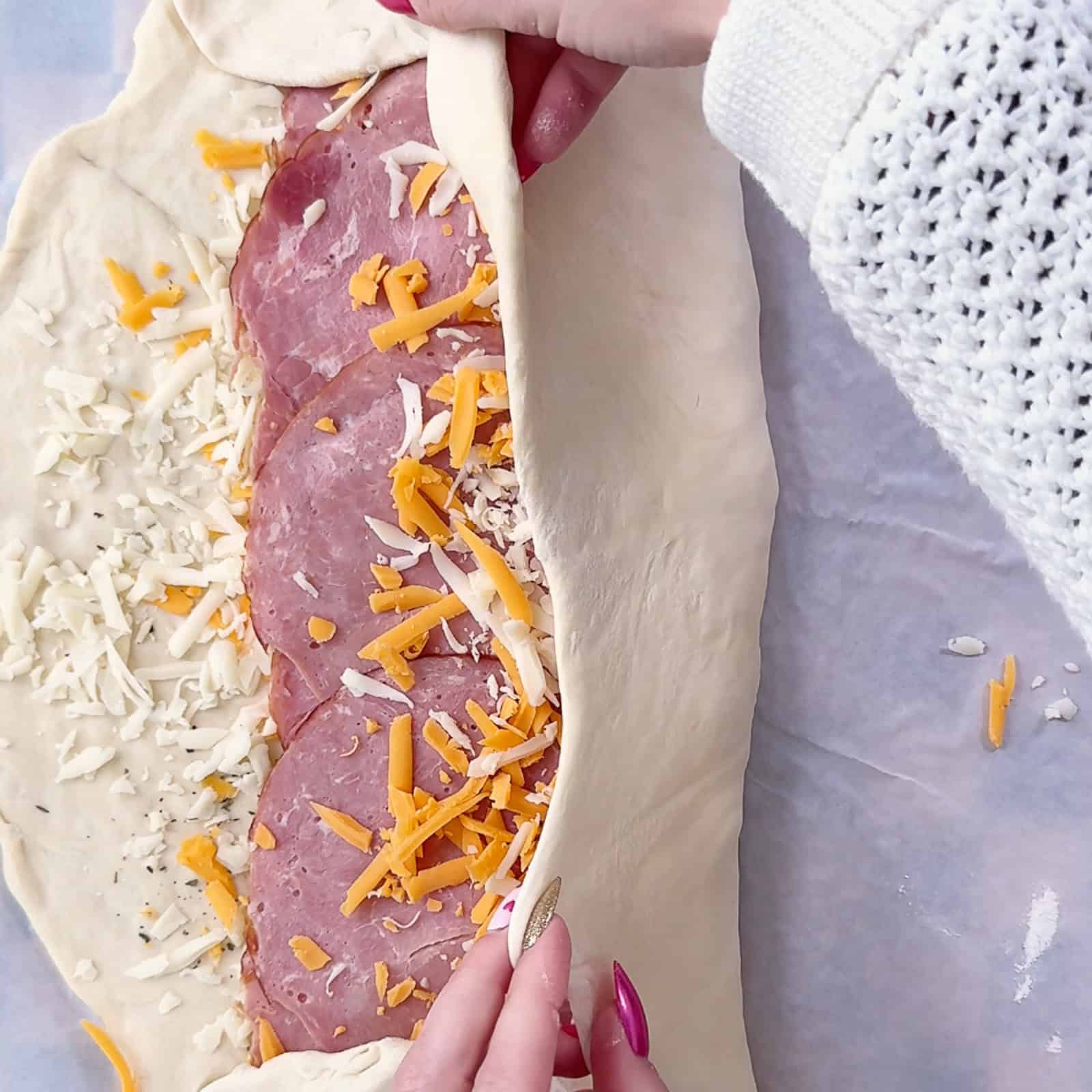 Folding pizza dough over ham and cheese to form a tight stromboli log