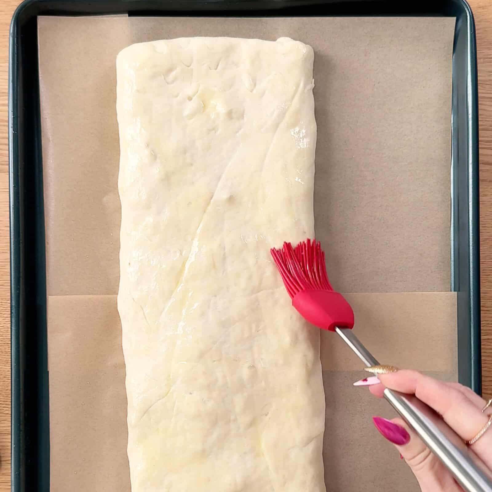 Brushing olive oil over the top of stromboli dough before baking