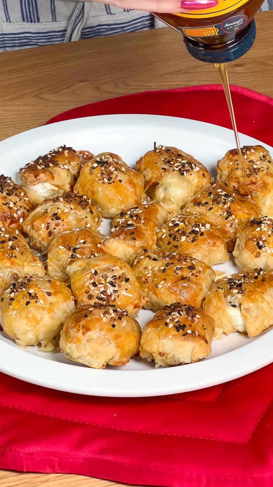 Honey being drizzled over warm puff pastry brie and fig bites