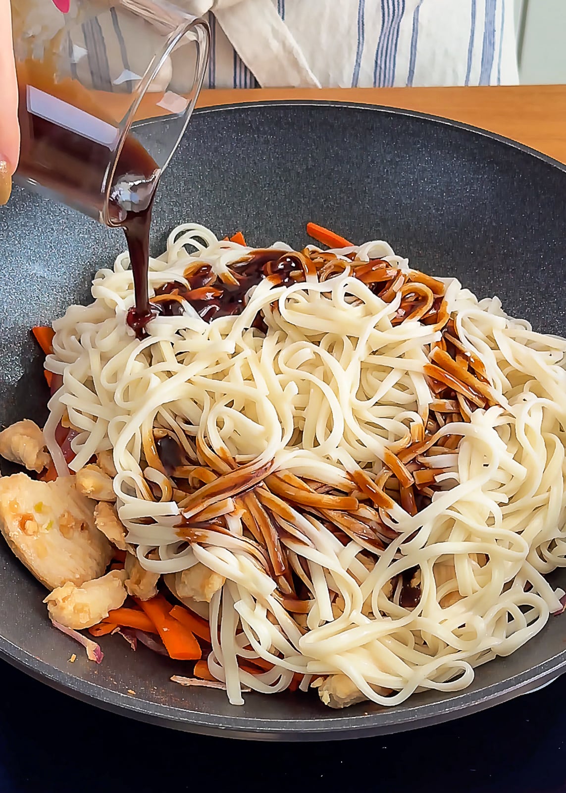 Pouring savory sauce over noodles in wok