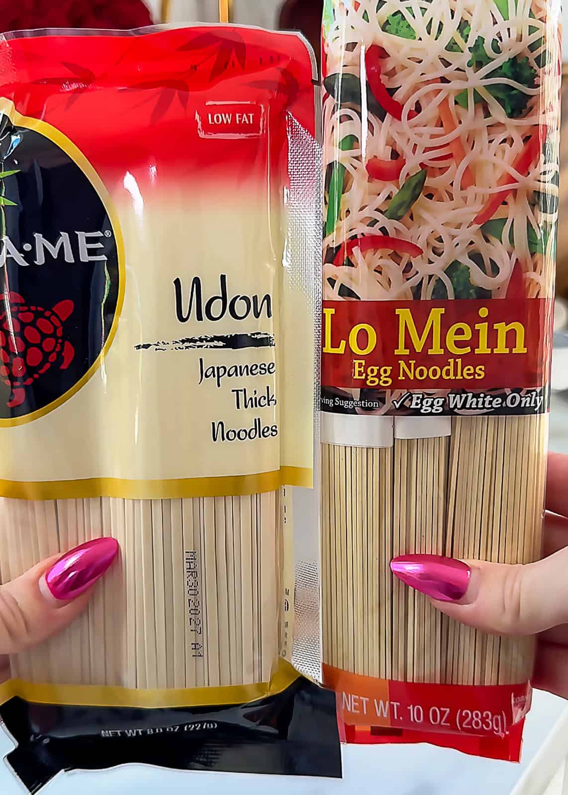 Hands holding thick udon noodles and thin lo mein noodles