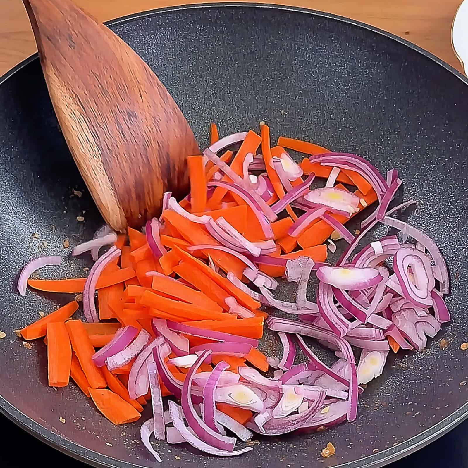 Carrots and red onion sautéing in wok