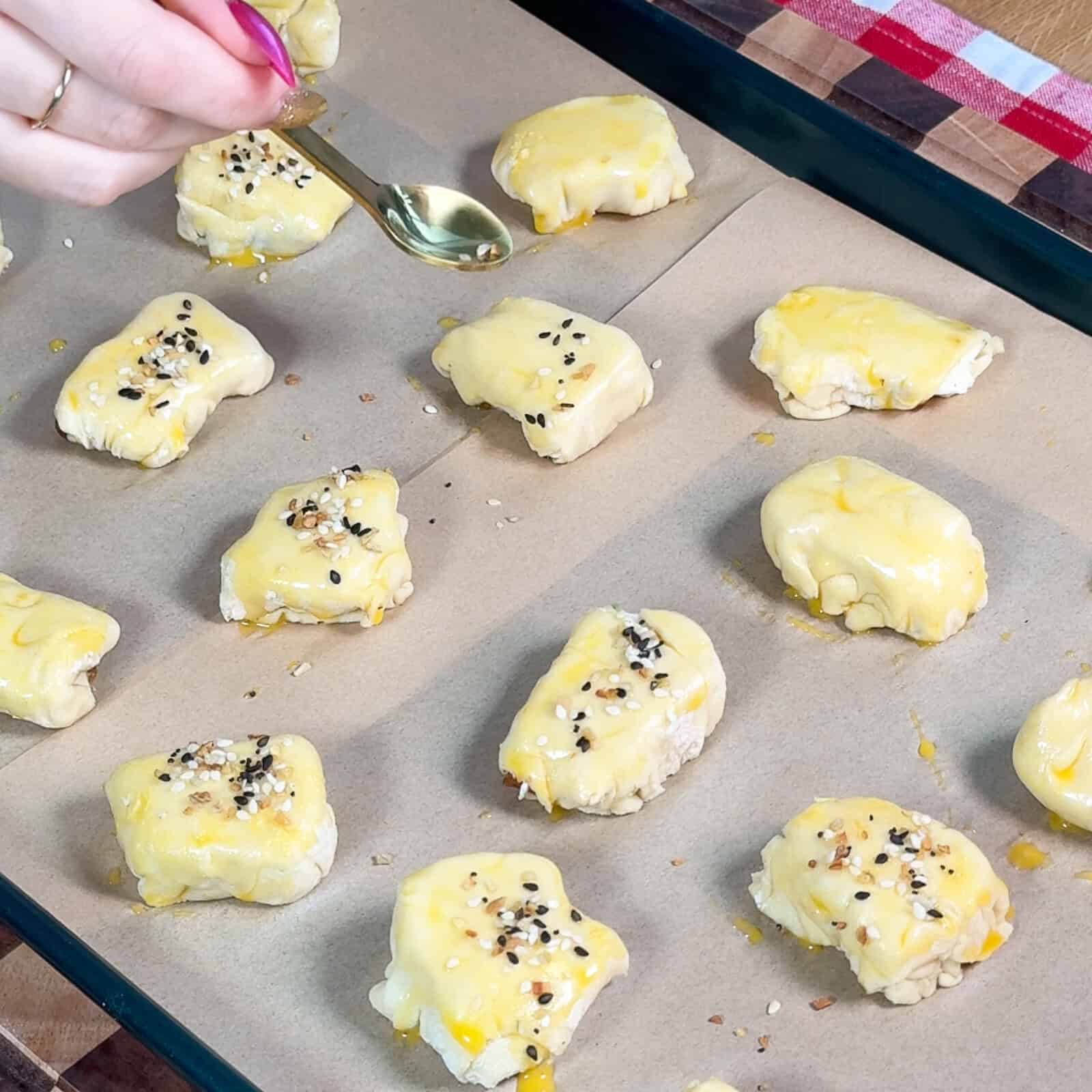 Brushing egg wash on puff pastry bites with everything seasoning