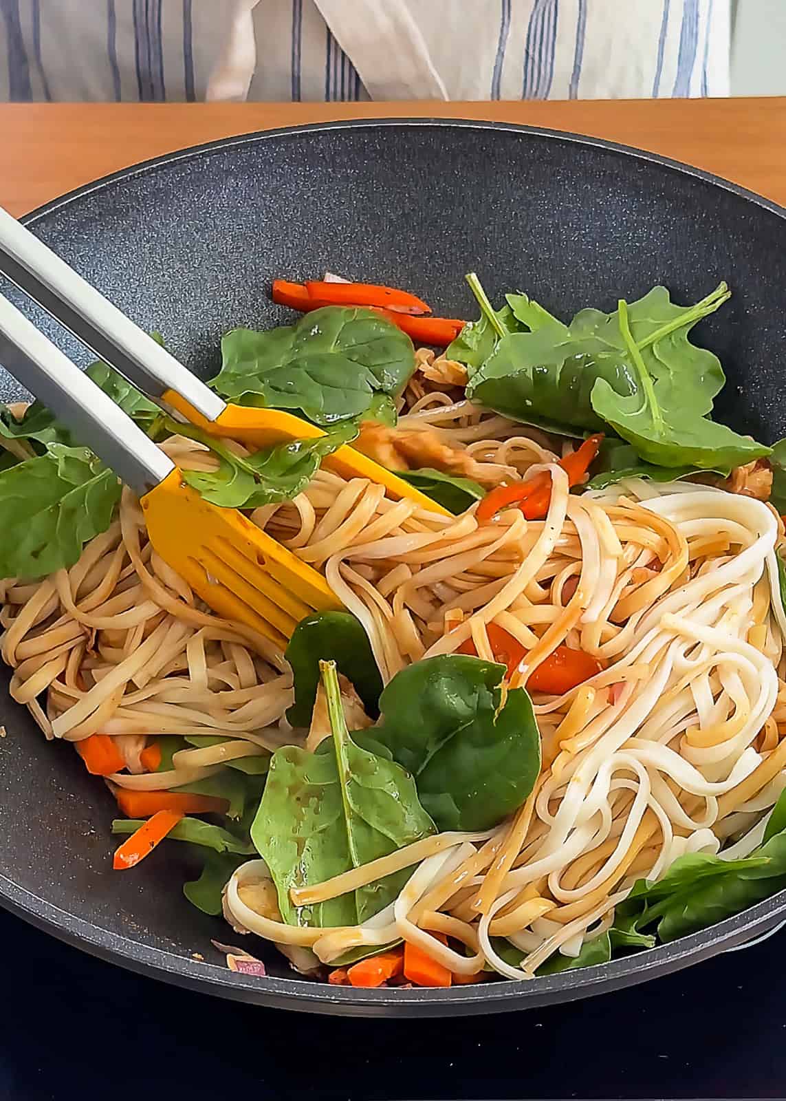Tongs tossing carrots and onions in stir fry