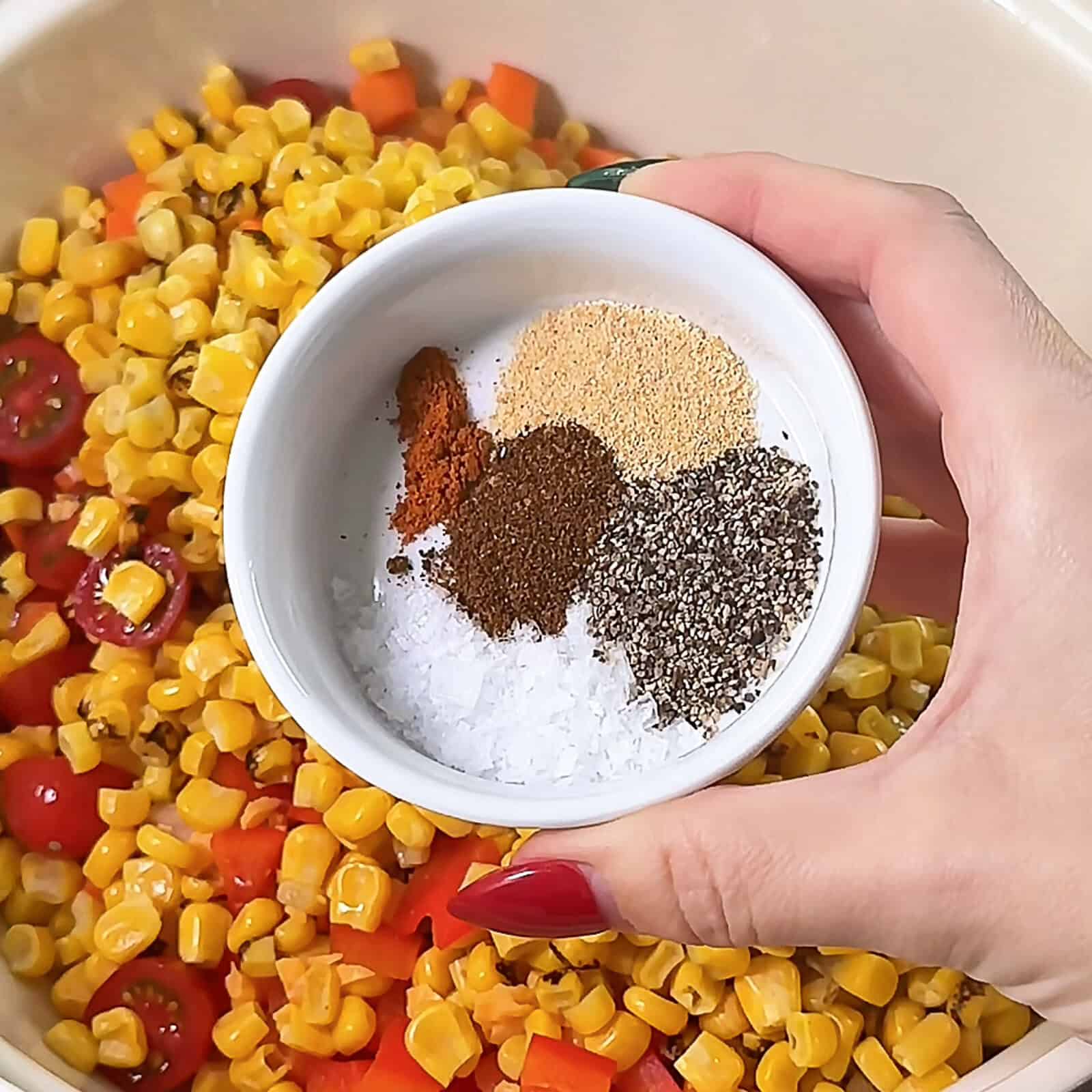 Sprinkling spices over Corn Salsa Dip in a mixing bowl