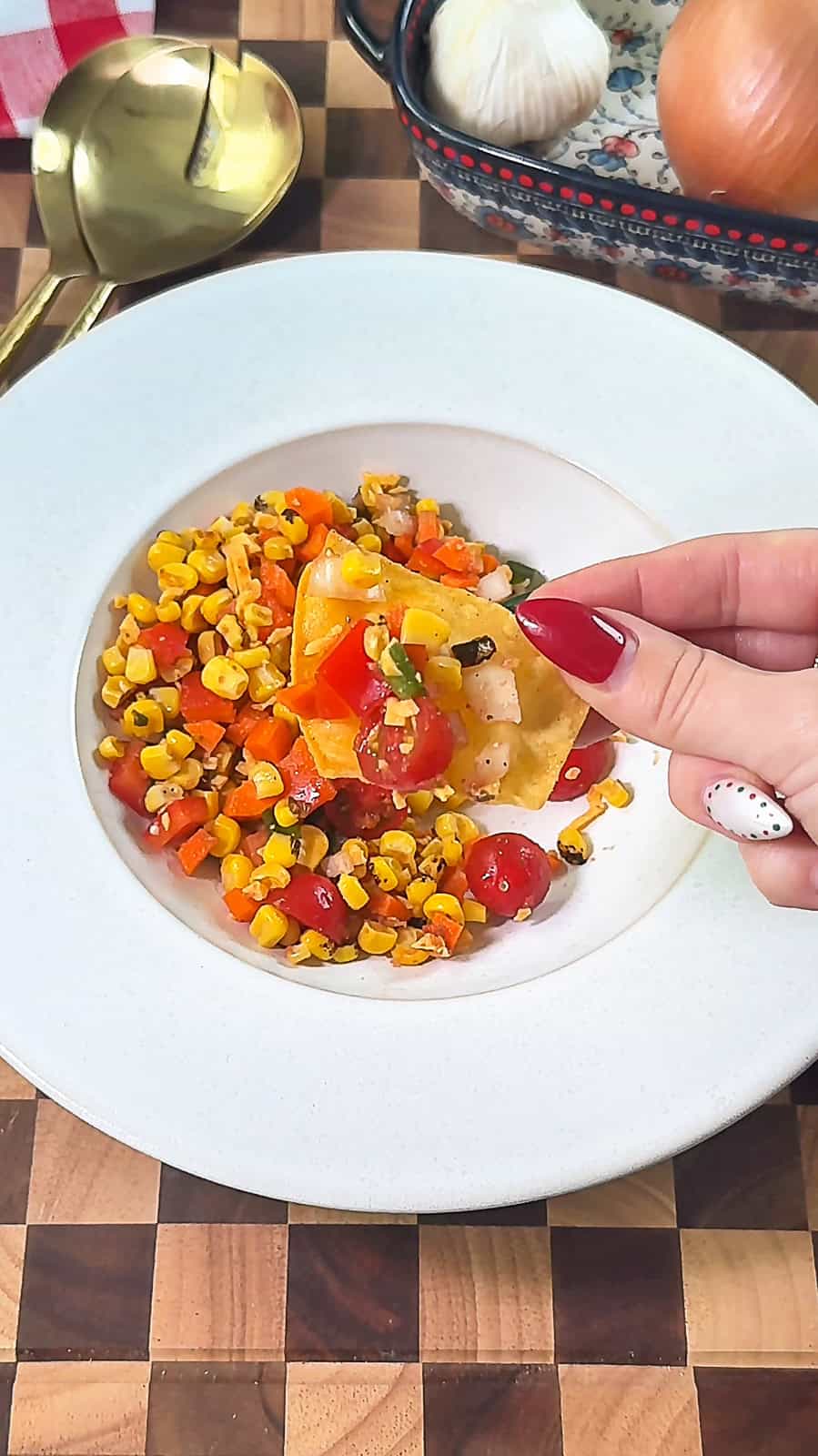 Hand holding tortilla chip over a bowl of Make-Ahead Corn Salsa Dip