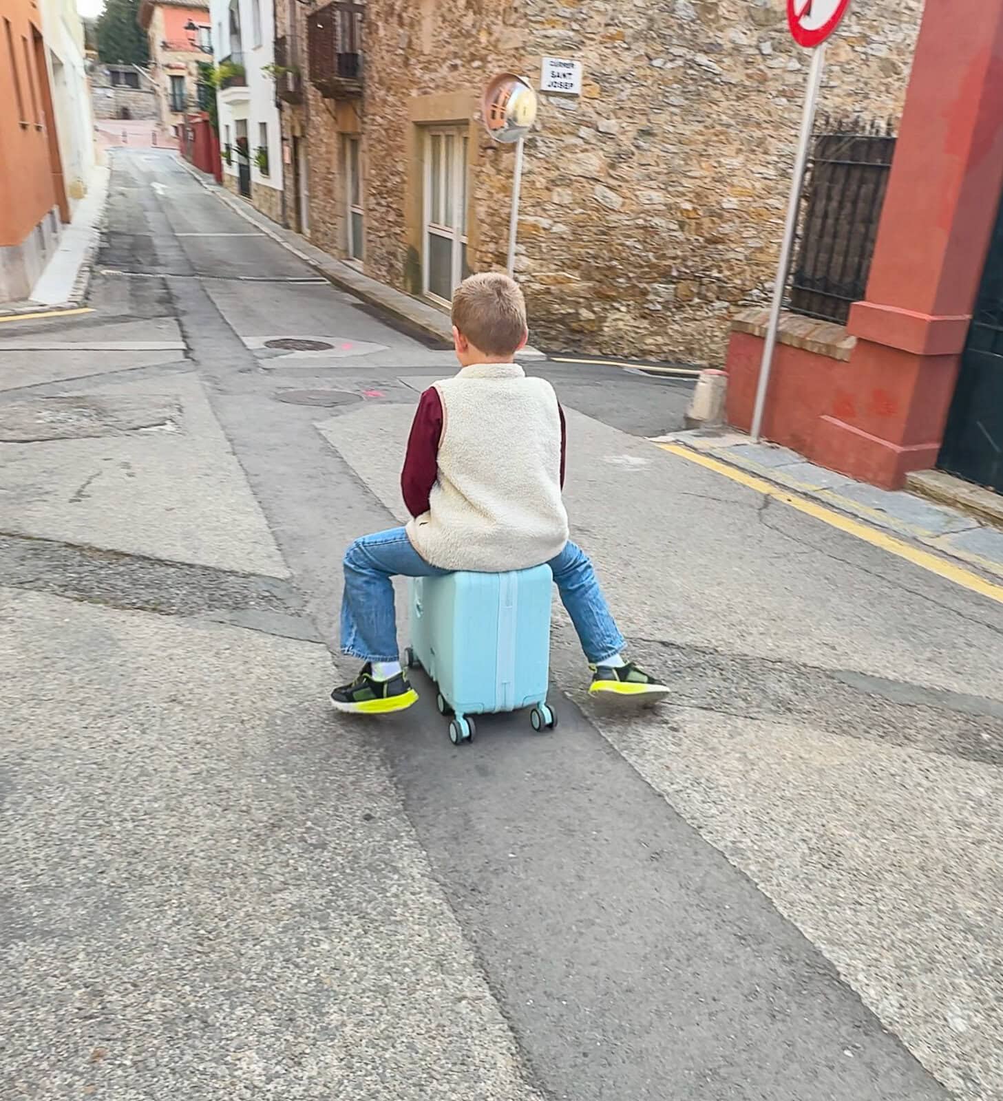 Child riding on small luggage in Spain with city background