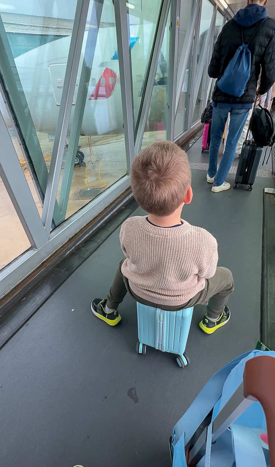 Child riding on small luggage while waiting in line to board plane
