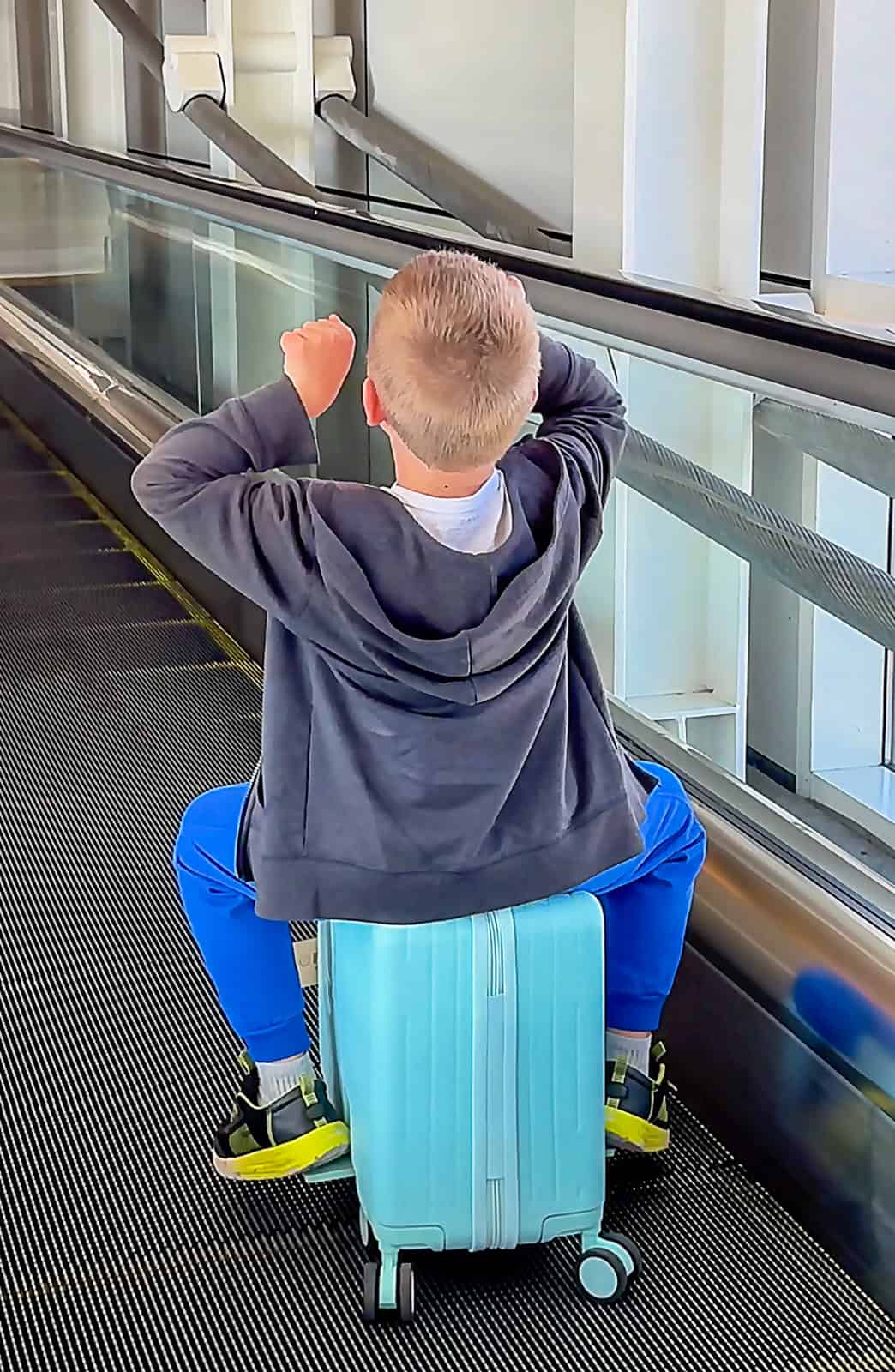 Child sitting on ride-on luggage at airport